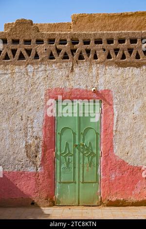 Porte en fer vert dans le mur d'une maison traditionnelle en boue et paille dans le village Merzouga dans le désert du Sahara, Drâa-Tafilalet, Errachidia, Maroc Banque D'Images