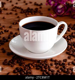 Une tasse en porcelaine blanche avec du café noir se tient sur une table en bois. Grains de café Banque D'Images