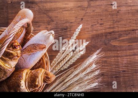 Vue rapprochée sur baguettes et croissants dans un panier en osier avec des épis de blé sur de vieilles planches de bois version horizontale Banque D'Images