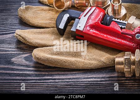 Gants de sécurité en cuir pour tuyaux connecteurs de plomberie en laiton sur planche de bois Banque D'Images