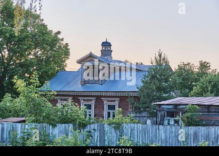 Yelabuga, Russie - 18 juin 2023 : vieille maison en bois derrière la clôture fanée.bandes de plaque en bois sculpté sur les fenêtres, balcon lucarne sur le toit, tourelle décorée avec esprit Banque D'Images