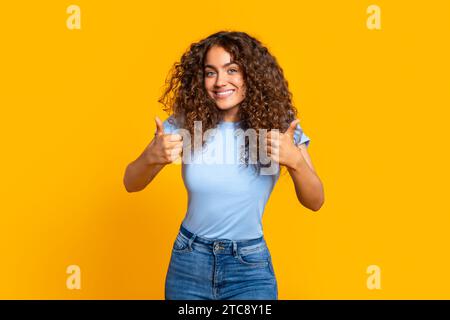 Heureuse femme frisée donnant deux pouces vers le haut sur le jaune Banque D'Images