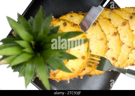 Ananas vibrant mûr tranché sur une assiette noire avec couteau et fourchette Banque D'Images