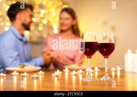 Couple en arrière-plan flou tenant les mains, verres à vin focalisés devant Banque D'Images