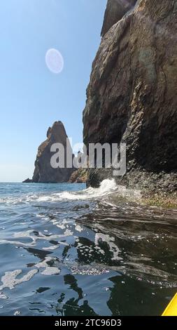 Kayak de mer rocaille les vagues. Kayak dans la mer par une journée ensoleillée le long de la côte et des rochers. vidéo verticale. Banque D'Images