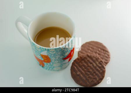 Une photo rapprochée d'une personne trempant un digestif au chocolat dans une tasse de thé. Banque D'Images