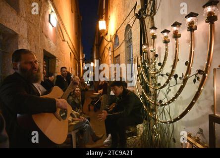 Jérusalem, Israël. 11 décembre 2023. Un rabbin ultra-orthodoxe joue de la guitare devant un grand hanukkiyah, la cinquième nuit de la fête juive de Hanukkah, la Fête des Lumières, à Nachlaot à Jérusalem, le lundi 11 décembre 2023. Les huit jours de la fête de Hanukkah commémorent la victoire des Maccabées sur le Royaume gréco-syrien et la nouvelle dédicace du second Temple. Photo de Debbie Hill/ crédit : UPI/Alamy Live News Banque D'Images