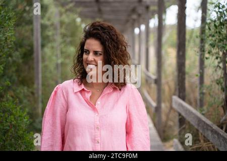 Portrait d'une jeune femme brune aux cheveux ondulés et une blouse rose regardant sur le côté dans un parc. Femme caucasienne Banque D'Images