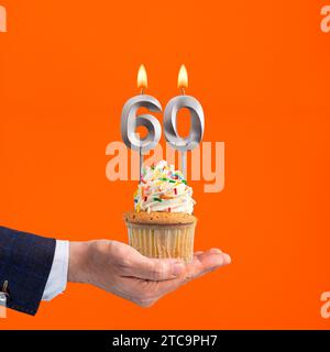 La main qui livre cupcake avec la bougie numéro 60 - anniversaire sur fond orange Banque D'Images