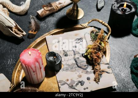 Attributs magiques de sorcière avec feuille de papier de sorcellerie, bougies allumées et fleurs sèches sur la table sombre, gros plan Banque D'Images