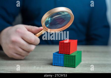 Examen des conteneurs de marchandises à travers une loupe. Étude de l'origine des marchandises et des itinéraires de livraison. La lutte contre le contournement des sanctions, Banque D'Images