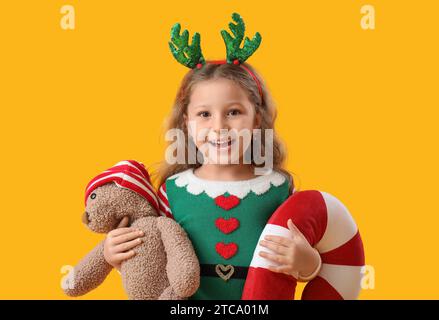 Jolie petite fille avec ours en peluche et coussin de Noël sur fond de couleur Banque D'Images