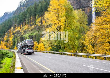 Transporteur classique grand rig car transporter semi-camion voiture de transport sur semi-remorque modulaire hydraulique fonctionnant sur la route sinueuse de l'autoroute avec le mountai rocheux Banque D'Images