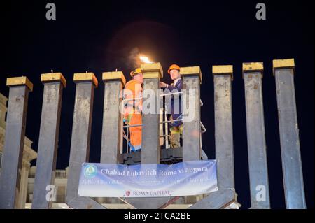 Rome, Italie. 10 décembre 2023. Deux ouvriers sur la grue allument le shamash, la bougie centrale de la grande Hanukkiah sur la Piazza Barberini à l'occasion de la célébration de Hanukkah à Rome.célébration de Hanukkah, la fête juive traditionnelle qui commémore la consécration du Temple de Jérusalem après les Maccabées, guerriers juifs, vaincu miraculeusement la puissante armée gréco-syrienne, organisée par le mouvement juif Chabad-Loubavitch de Rome.Chabad, acronyme hébreu pour sagesse, compréhension et connaissance, est le mouvement international né des Juifs Lubavitcher deux siècles Banque D'Images