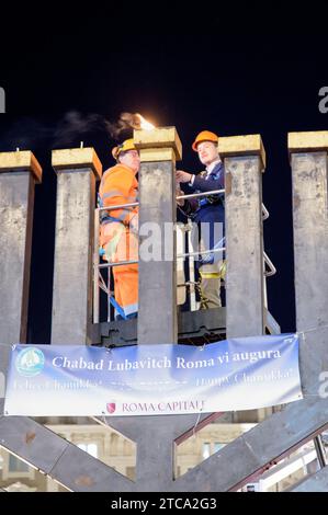 Rome, Italie. 10 décembre 2023. Deux ouvriers sur la grue allument le shamash, la bougie centrale de la grande Hanukkiah sur la Piazza Barberini à l'occasion de la célébration de Hanukkah à Rome.célébration de Hanukkah, la fête juive traditionnelle qui commémore la consécration du Temple de Jérusalem après les Maccabées, guerriers juifs, vaincu miraculeusement la puissante armée gréco-syrienne, organisée par le mouvement juif Chabad-Loubavitch de Rome.Chabad, acronyme hébreu pour sagesse, compréhension et connaissance, est le mouvement international né des Juifs Lubavitcher deux siècles Banque D'Images