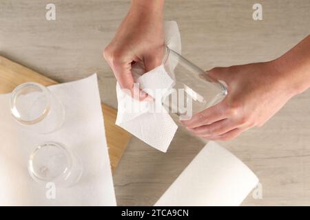 Femme essuyant le verre avec essuie-tout à la table en bois, vue de dessus Banque D'Images