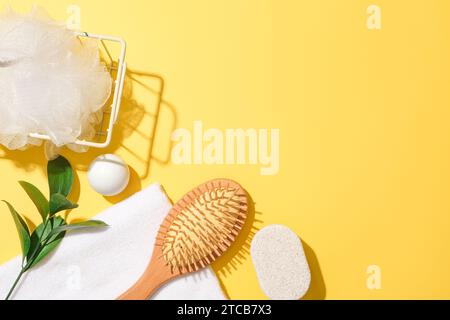 Une éponge de bain dans un panier en fer, des feuilles vertes, une boule blanche, une serviette, du savon et un peigne démêlant sont décorés dans le coin gauche sur un fond jaune Banque D'Images