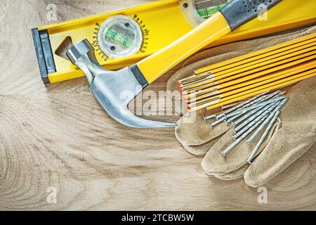 Gants de protection en cuir de niveau bâtiment clous en métal de marteau de pince de mètre de bois sur le concept de construction de planche de bois Banque D'Images