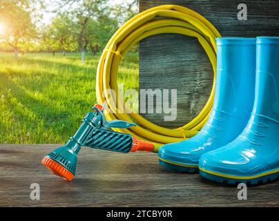 Outils de jardin tuyau d'arrosage avec spray Gan pluie bottes en caoutchouc sur la terrasse dans le jardin ensoleillé de printemps Banque D'Images