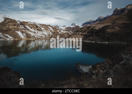 Lac de haute montagne dans le nord du Caucase, entouré de rochers épiques et d'un ciel étoilé d'hiver brillant au lever du soleil. Paysage de nuit sur longue exposition. Froid Banque D'Images