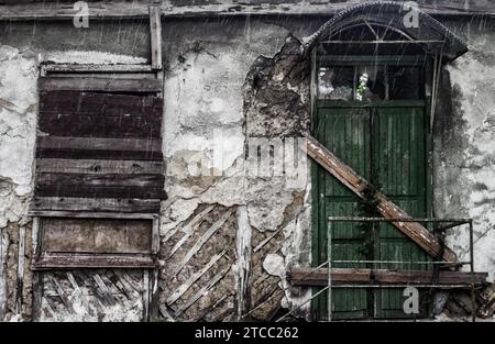 Vieux bâtiment détruit avec une fenêtre barrée et une porte sous la pluie Banque D'Images