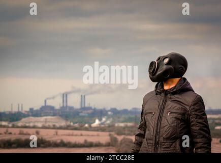 Homme dans un masque à gaz au milieu de la fumée des tuyaux d'usine se ferment Banque D'Images