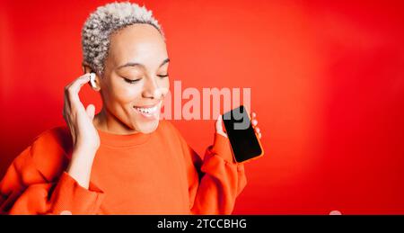 Heureuse jeune femme dansant tout en portant des écouteurs sans fil dans un studio. Femme écoutant ses playlists musicales préférées. Banque D'Images