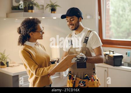 Smilng jeune femme signant le document tout en communiquant avec bricoleur à la cuisine Banque D'Images