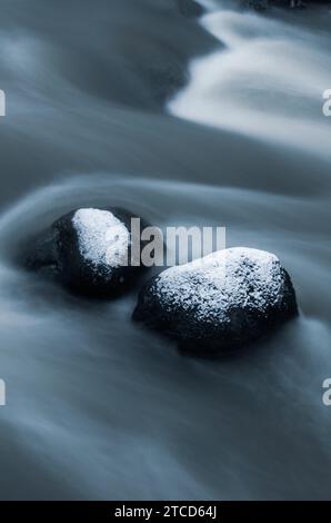 Rivière glacée avec de l'eau qui coule et des rochers enneigés en hiver. Banque D'Images