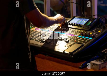 technicien du son méconnaissable réglant les niveaux sur une console de mixage multipiste dans la salle de contrôle pendant un événement Banque D'Images