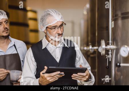 Viticulteur professionnel travaillant dans une grande usine de vinification moderne alcool alcool alcool industrie du contrôle de la qualité et de la fermentation surveillent la couleur vintage à Banque D'Images