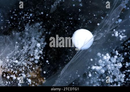 Les bulles de méthane, les fissures et la neige à la surface du lac Baïkal créent un motif de glace inhabituel comme la nuit de lune. Texture hivernale. Fond d'hiver abstrait. Haut Banque D'Images