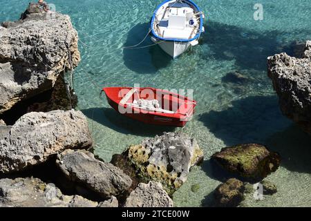 Petit bateau rouge nommé 'Scuccidda' attaché avec des cordes entre les rochers dans la baie de la ville sicilienne de Levanzo Banque D'Images