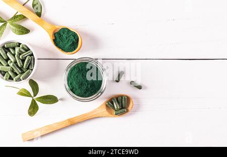 Poudre verte et comprimés d'algues spiruline dans des pots en verre et cuillère sur fond en bois blanc. Vue de dessus. Un espace de copie. teneur élevée en multivitamines Banque D'Images