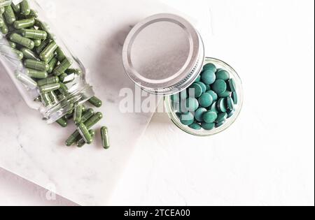 Comprimés ronds d'algues spiruline naturelle bleu-vert dans le verre de banque sur fond blanc. pot médical avec capsules d'algues. Compléments alimentaires naturels Banque D'Images