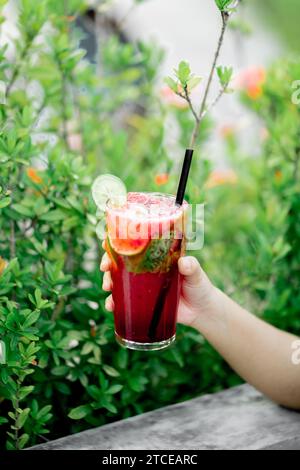 Une main de personne tenant un verre de boisson infusée aux fruits à l'extérieur. Banque D'Images