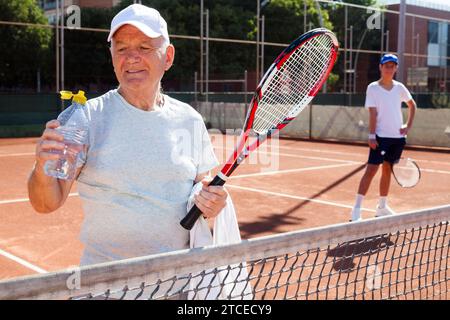 Un homme âgé boit de l'eau sur un court de tennis Banque D'Images