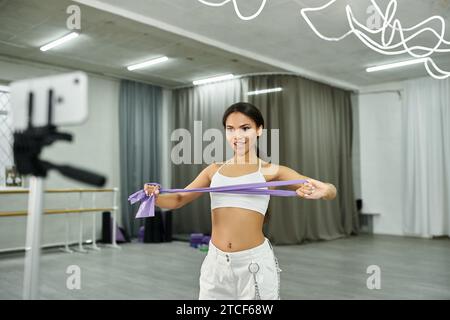 danseuse afro-américaine souriante dans la formation de vêtements de sport blancs avec des élastiques dans la salle de danse Banque D'Images