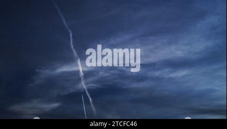 Jet commercial à haute altitude laisse un contrail net-nouveau le long du chemin d'un sentier de condensation persistante plus ancien. Banque D'Images