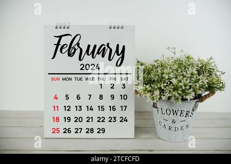 Février 2024 calendrier mensuel avec plante artificielle verte dans un vase en métal sur fond en bois Banque D'Images