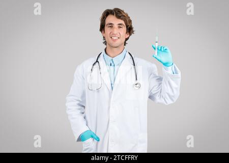 Homme positif médecin en manteau blanc, gants de protection à l'aide de la seringue, recommandant la vaccination sur fond gris Banque D'Images