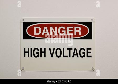 Danger panneau d'avertissement en plastique haute tension isolé et fixé à un mur blanc avec des goupilles à emboîter. Concept de sécurité électrique. Banque D'Images