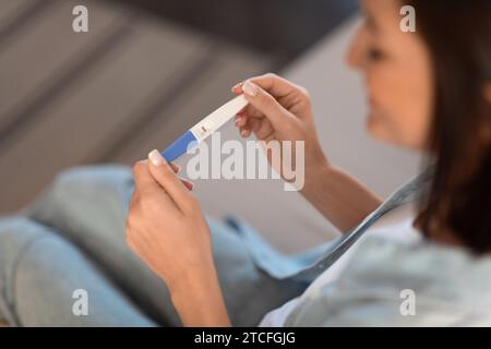 Femme enceinte souriante tient un test de grossesse positif assis à l'intérieur, recadré Banque D'Images