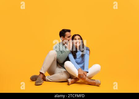 Homme assis chuchote dans l'oreille de la femme, souriant avec un regard de secret et de joie partagés Banque D'Images