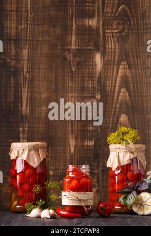 Tomates cerises en conserve dans des pots fermés et ouverts, épices et herbes pour marinade sur fond en bois. Banque D'Images