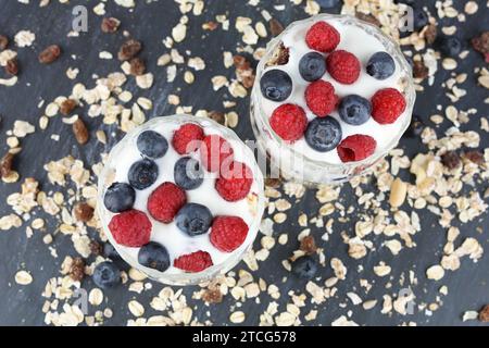 Muesly avec des framboises et des bleuets dans deux verres sur fond sombre. Banque D'Images