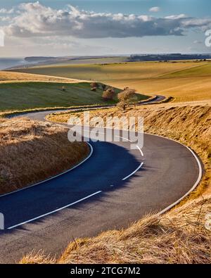 Route rurale sinueuse menant à travers la campagne baignée de soleil avertissant dans le Sussex, en Angleterre. Banque D'Images