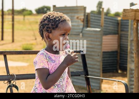 jeune fille africaine du village mangeant un lollypop, elle est située sur un banc d'une charrette d'âne à l'extérieur Banque D'Images