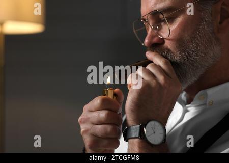 Homme barbu allumant un cigare à l'intérieur, gros plan. Espace pour le texte Banque D'Images