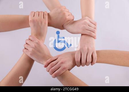 Concept d'inclusion. Les gens se tenant la main ensemble autour du symbole international de l'accès ensemble sur fond blanc, vue de dessus Banque D'Images